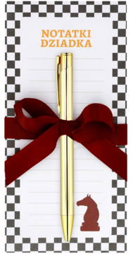 Złoty długopis na białym notesie "Notatki Dziadka" z szachową obwódką i figurą konia, związany czerwoną kokardą.