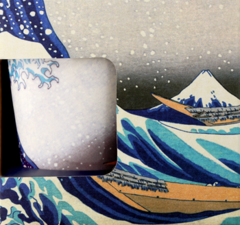 Biały ceramiczny kubek z niebieskimi falami i kropkami, widoczny w oknie ekspozycji, na tle „Wielkiej Fali”.