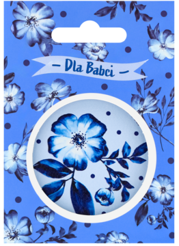 Niebieska torebka prezentowa w kwiaty, z białym napisem "Dla Babci" i okrągłym wycięciem z niebieskim kwiatem.