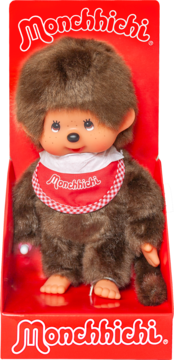 Monchhichi pluszowa lalka z brązowego futra, beżowa twarz, w czerwonym opakowaniu, z czerwono-białym śliniakiem.