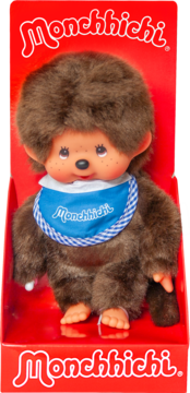 Pluszowa lalka Monchhichi w czerwonym pudełku, brązowa, z winylową twarzą i dłońmi, w niebieskim śliniaku.