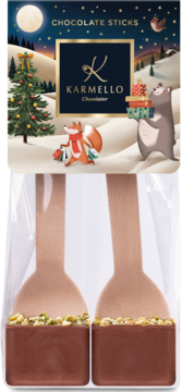 Dwa Karmello Chocolate Sticks z pistacjami na drewnianych łyżeczkach, na tle świątecznego opakowania z misiem i lisem.
