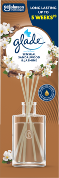 Glade dyfuzor zapachowy Sensual Sandalwood & Jasmine, szklana butelka z patyczkami, brązowe tło, białe kwiaty.