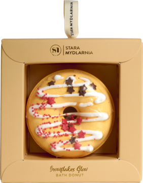 Żółty musujący donut do kąpieli o zapachu pomarańczy i cynamonu, z białą polewą, w beżowym pudełku z okienkiem.