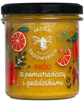 Miód Pasieki Sadowskich z pomarańczą i goździkami w słoiku, czarna zakrętka, świąteczna etykieta z pszczołą i owocami.