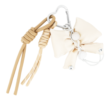 Eloy brelok: jasnobeżowa materiałowa kokarda, pleciony sznurek z frędzlami, metalowy karabińczyk i kółko.