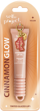 Selfie Project Charming Lip Oil Cinnamon Glow w beżowej tubce, z złotym brelokiem, w blistrze. Widok z przodu.