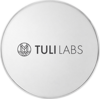 Okrągłe, jasnoszare wieczko pudru sypkiego Tuli Labs Light z matowym wykończeniem i logo firmy.
