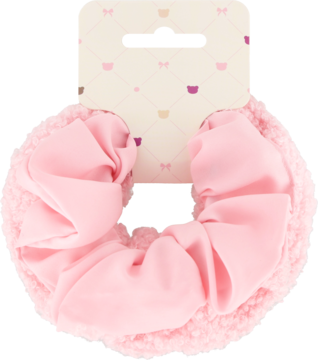 Puchata, różowa scrunchie Eloy z falbankami, na jasnej tekturze z wzorem serc. Widok z przodu.