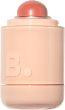 Kremowy róż w sztyfcie B. w matowej, brzoskwiniowej obudowie z widoczną kopułą koralowego bluszu, ujęcie z przodu.