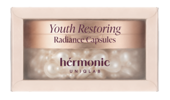 Hermonic Youth Restoring Radiance Capsules w jasnoróżowym pudełku z przezroczystym okienkiem, widoczne perłowe kapsułki.