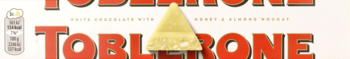 Toblerone biała czekolada z nugatem miodowo-migdałowym, widok na fragment opakowania i trójkątny kawałek.