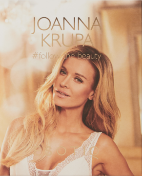 Joanna Krupa w reklamie perfum #followme beauty SOIR. Blondynka w białym topie, uśmiechnięta, ciepłe tło.