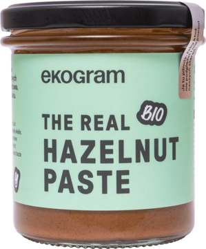 Szklany słoik organicznej pasty Ekogram BIO The Real Hazelnut Paste z zieloną etykietą i czarną zakrętką, z przodu.