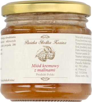 Szklany słoik miodu kremowego z malinami Pasieka Słodka Kraina, z kremową etykietą i złotą nakrętką.