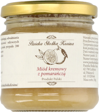 Szklany słoik kremowego miodu z pomarańczą "Pasieka Słodka Kraina" z ilustracją pomarańczy na białej etykiecie.