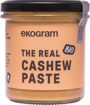 Ekologiczna pasta ekogram The Real Cashew Paste w szklanym słoiku, widok z przodu na beżowej etykiecie.