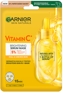 Żółta maska Garnier Vitamin C na tkaninie, z buteleczką serum, na tle cytryn, widok z przodu.