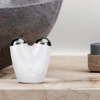 Biały GESKE lifting do twarzy 6w1 anti-aging z mikroprądem, widok z przodu, srebrne głowice, na marmurze.