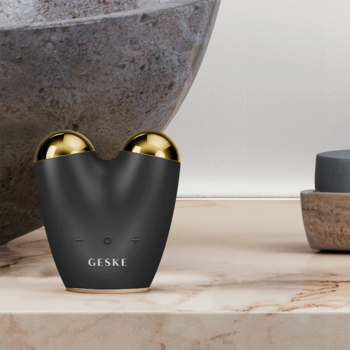 GESKE 6w1 mikroprądowy masażer do twarzy, czarny ze złotymi głowicami, na jasnym marmurowym blacie.