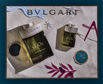 Zestaw męskich perfum Bvlgari Man Wood Essence 100ml i 15ml na tle piasku z letnimi ozdobami.