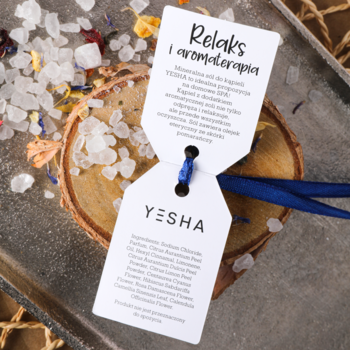 Aromatyczna sól mineralna Yesha do kąpieli z barwnymi płatkami kwiatów, rozsypana na plastrze drewna z dwoma tagami.