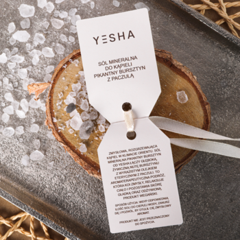 Sól mineralna YESHA Pikantny Bursztyn z Paczulą, zbliżenie na sypkie kryształy z etykietą na drewnie.