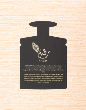 Widok z przodu czarnej etykiety Ard Al Zaafaran Riqqa, w kształcie butelki z logo i listą składników, na jasnym drewnie.