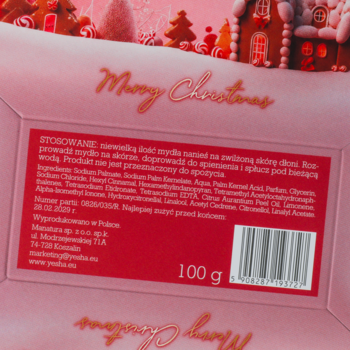Tył czerwonego opakowania mydła 'Merry Christmas' z listą składników i kodem kreskowym, na tle domku z piernika.