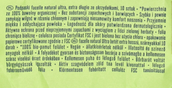 Zbliżenie na biały, szczegółowy opis podpasek facelle na jasnym, zielonym tle opakowania produktu.