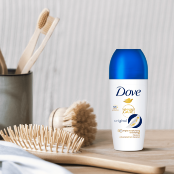 Antyperspirant Dove Original w białej butelce z niebieską nakrętką, na drewnianym blacie z bambusowymi szczotkami.