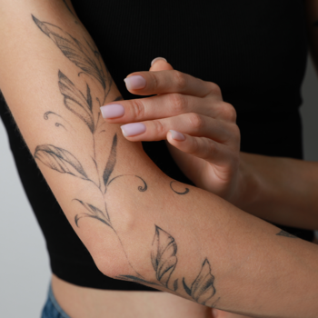 Zbliżenie na damskie przedramię z tatuażem liści, wskazujące na pielęgnację Mistero Milano dr Tattoo After Care.