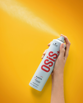 Lakier do włosów OSiS+ Elastic w białej butelce, z mgiełką, trzymany ręką na żółtym tle.