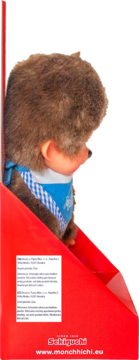 Monchhichi maskotka, brązowe futerko, niebieska chustka, w czerwonym opakowaniu, widok z boku z etykietą produktu.