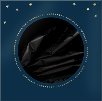 Pognieciona czarna tekstura, przypominająca folię, w złotym kole z napisem 'HANDMADE' na tle granatowego nieba z gwiazdami.