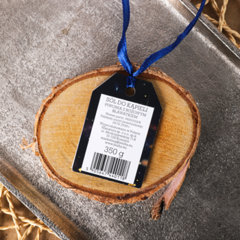 Sól do kąpieli Yesha 350g, widok etykiety z niebieską wstążką na plastrze drewna, metaliczne tło.