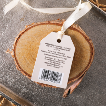 Zbliżenie na białą zawieszkę z tyłu opakowania soli mineralnej Yesha, leżącą na drewnianym krążku.