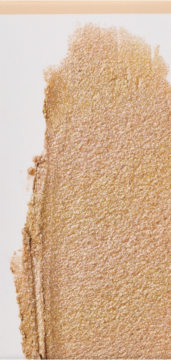 Zbliżenie na złocisty rozświetlacz z efektem glass skin, widoczne na białym tle, z delikatną, kremową teksturą.