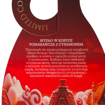 Czerwona, dekoracyjna etykieta mydła w kostce "Pomarańcza z Cynamonem Limited Co" na ciemnym tle. Widoczne świąteczne domki.