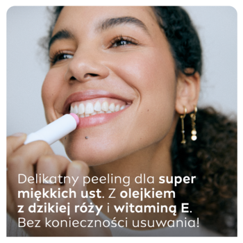Uśmiechnięta kobieta aplikuje NIVEA peeling do ust dzika róża w sztyfcie, bez konieczności usuwania.