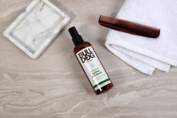 Bulldog Original Sea Salt Spray do włosów w brązowej butelce z zieloną etykietą, na marmurze z grzebieniem i ręcznikiem.