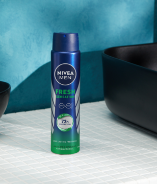 Niebieski antyperspirant w sprayu Nivea Men Fresh Sensation, z zielonym dołem i napisem 72h, stoi na białych kafelkach.