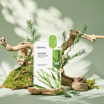 Biała maseczka Teatree Essential Mask w płachcie, z ilustracją liści, na tle mchu i gałęzi w słońcu.