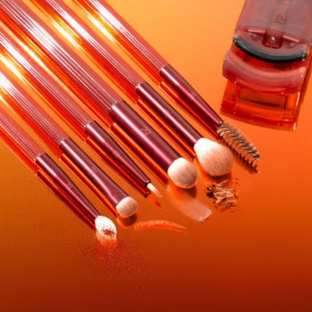 Real Techniques Solar Power eye set: 6 orange brushes & mini curler on reflective amber. Scattered makeup powder.