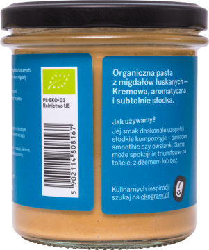 Tył słoika BIO pasty z łuskanych migdałów Ekogram. Kremowa, jasnobrązowa pasta, niebieska etykieta, kod.