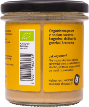 Tył szklanego słoika organicznej pasty sezamowej, z żółtą etykietą, tekstem i zielonym logo bio.