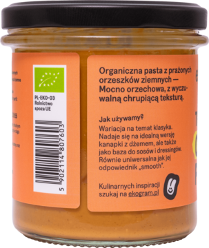 Tył szklanego słoika ekologicznej pasty z prażonych orzechów ziemnych, chrupiącej, z pomarańczową etykietą.
