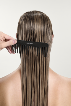 Widok od tyłu: dłoń czesze mokre, długie, jasne włosy czarnym grzebieniem. Rozjaśniająca odżywka do włosów.