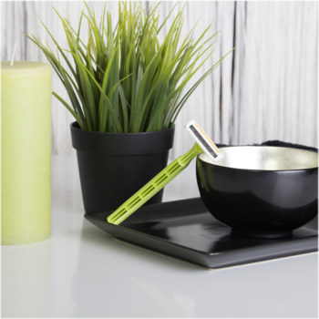 Zielona jednorazowa maszynka BIC Pure Lady z potrójnym ostrzem, na czarnej tacy, otoczona świecą i rośliną.