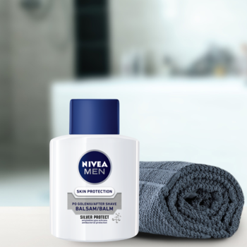 NIVEA MEN Silver Protect Balsam po goleniu w białej butelce z niebieską nakrętką, obok szary ręcznik.
